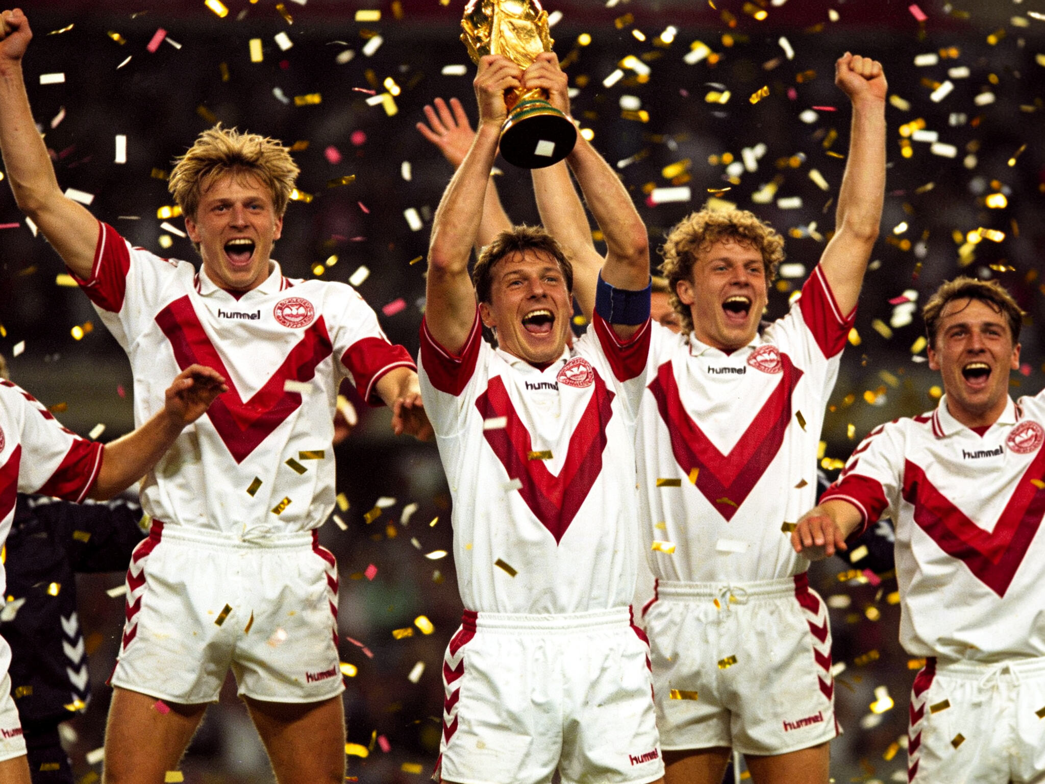 The victorious Denmark national football team celebrating with the UEFA Euro 1992 trophy, showcasing their iconic white home jerseys with bold red Hummel chevrons across the chest, a symbol of football's greatest underdog story.The victorious Denmark national football team celebrating with the UEFA Euro 1992 trophy, showcasing their iconic white home jerseys with bold red Hummel chevrons across the chest, a symbol of football's greatest underdog story.