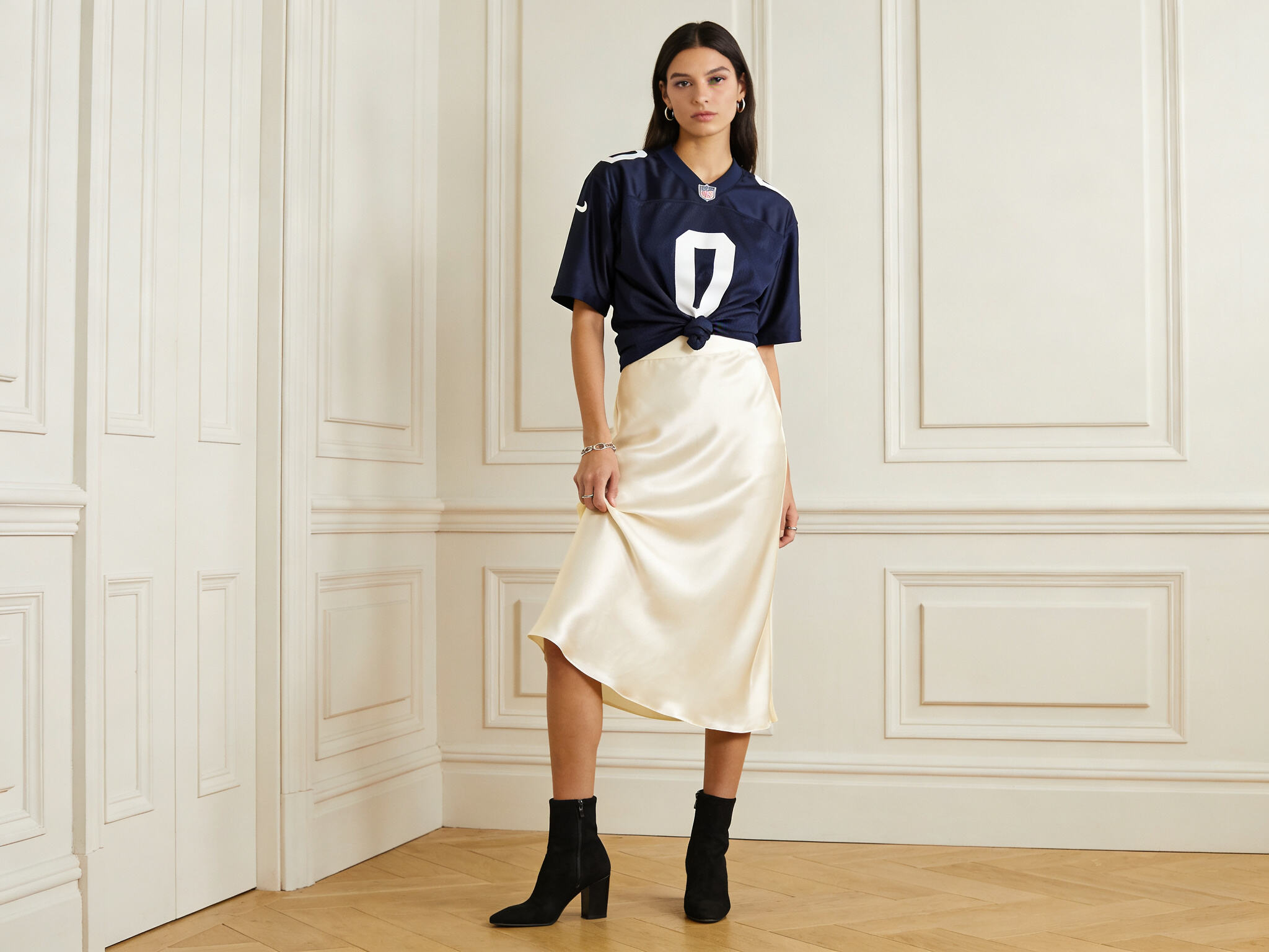 A person wearing a French navy jersey tucked into a cream-colored satin midi skirt, paired with minimalist jewelry and ankle boots.